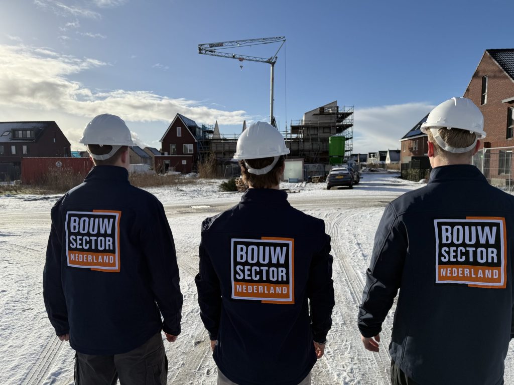 Drie vakmensen van Bouwsector Nederland in werkjas met helm bij woningen in aanbouw