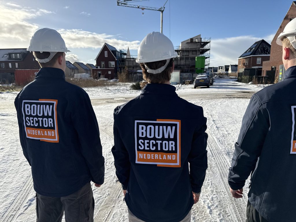 Drie mannen in werkjas met het logo van Bouwsector Nederland voor een rij huizen in aanbouw